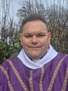 A selfie of Ross wearing a purple robe, with trees in the background.