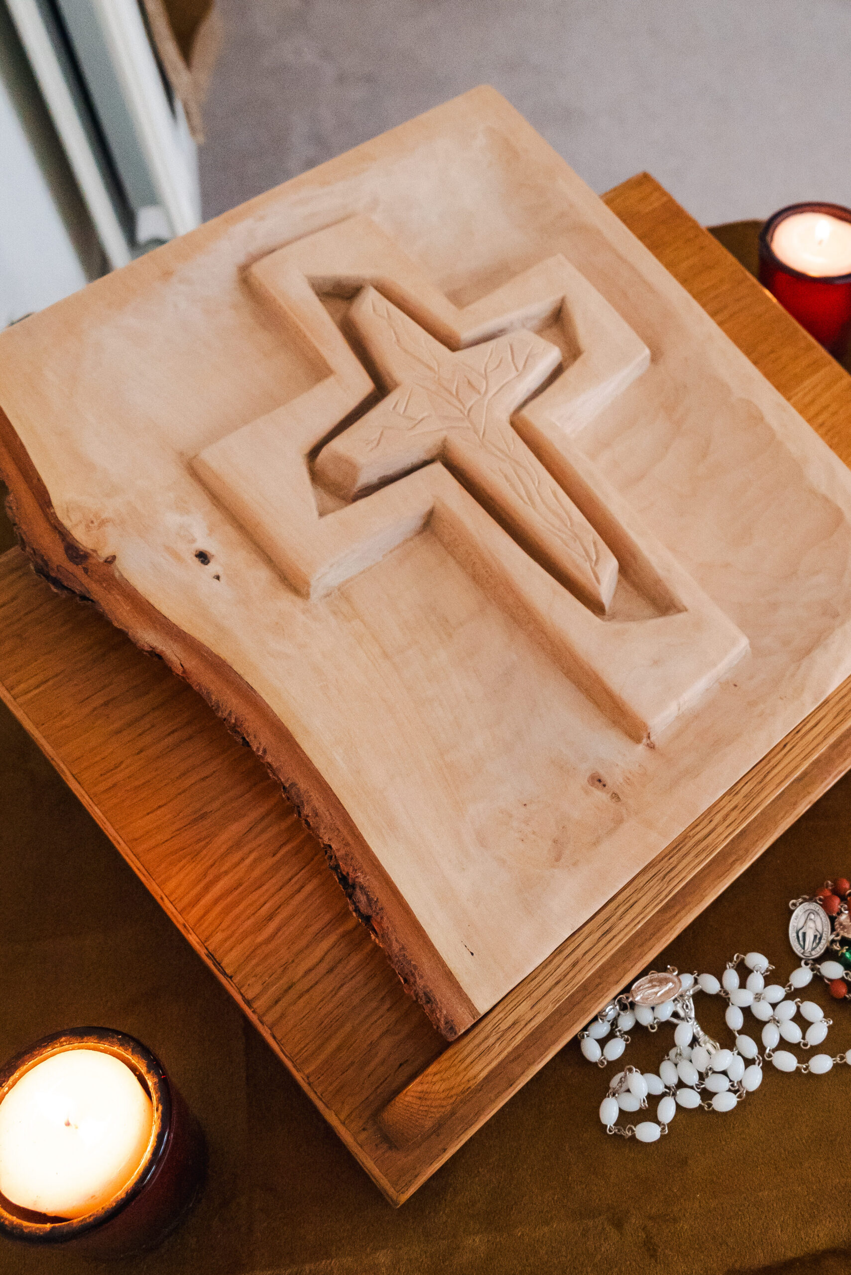 A wooden carving of a cross, held within a square wooden block, sits on a table.