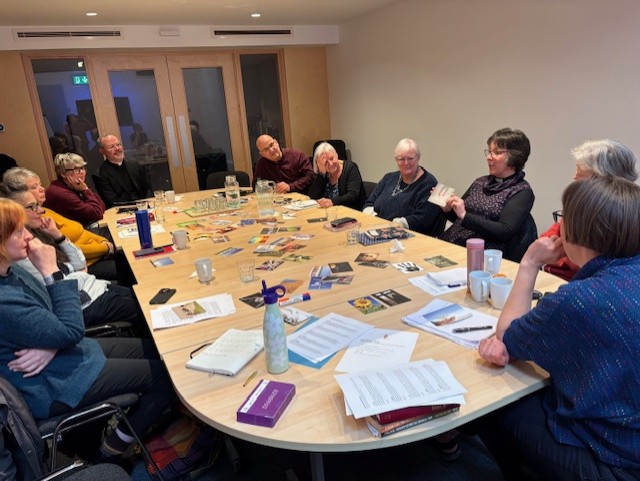Nine people are gathered around a table, with books and learning resources spread across the table.