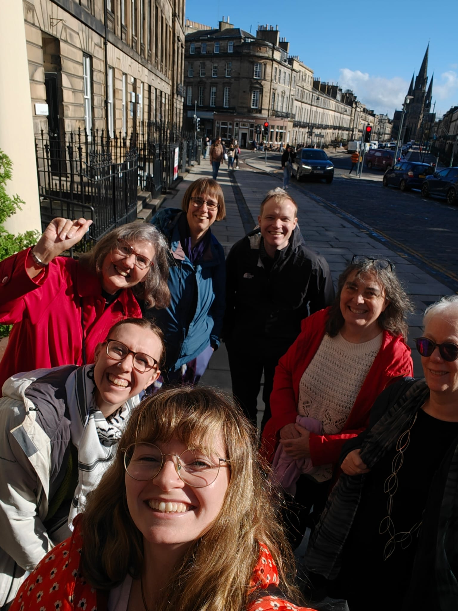 The SEI team, joined by the SEI Chaplain, are standing on the sidewalk, smiling and taking a selfie. St. Mary's Cathedral is in the background.